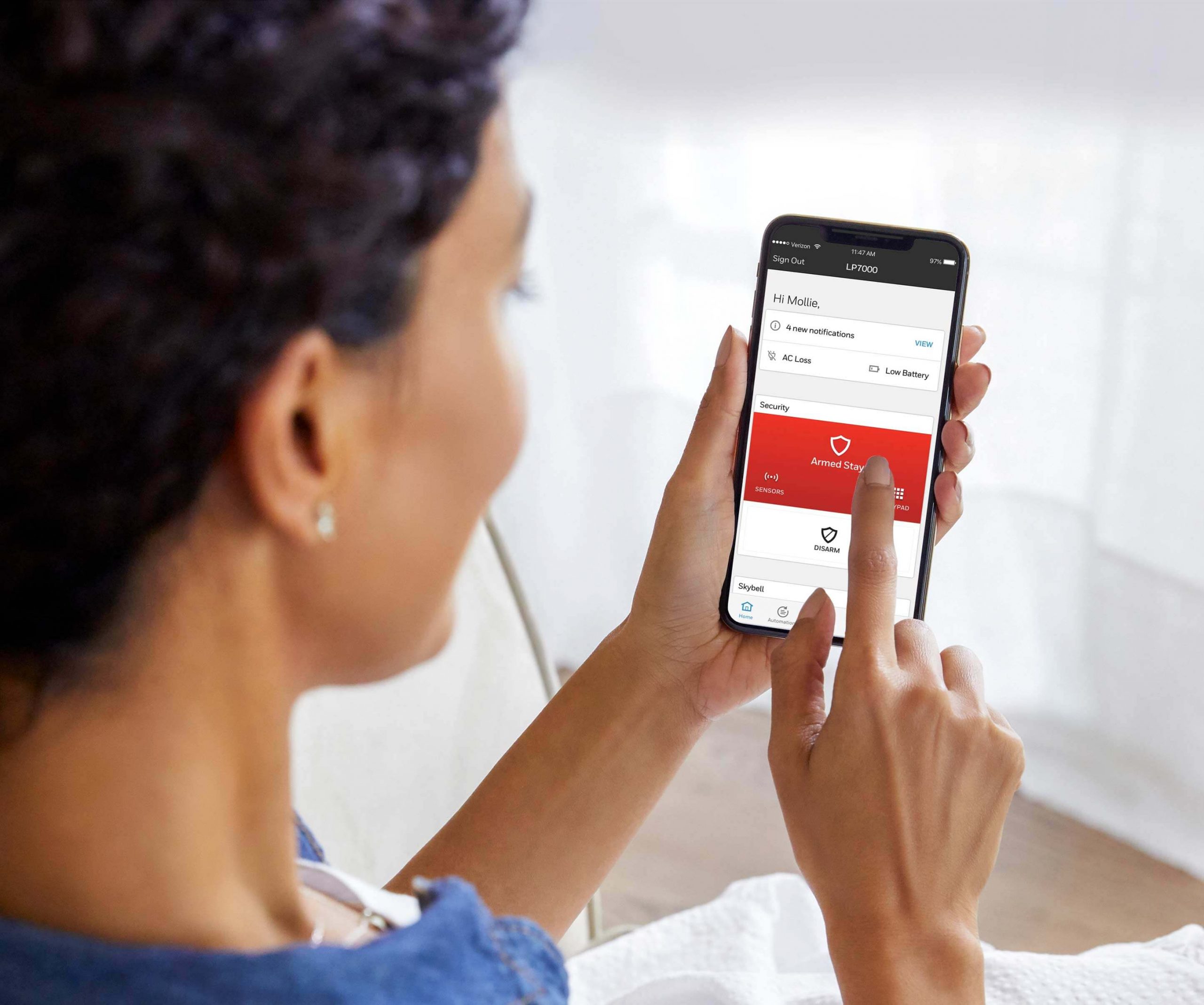A woman uses the Total Connect App on her mobile device to add remote access to her Honeywell Ademco alarm system.