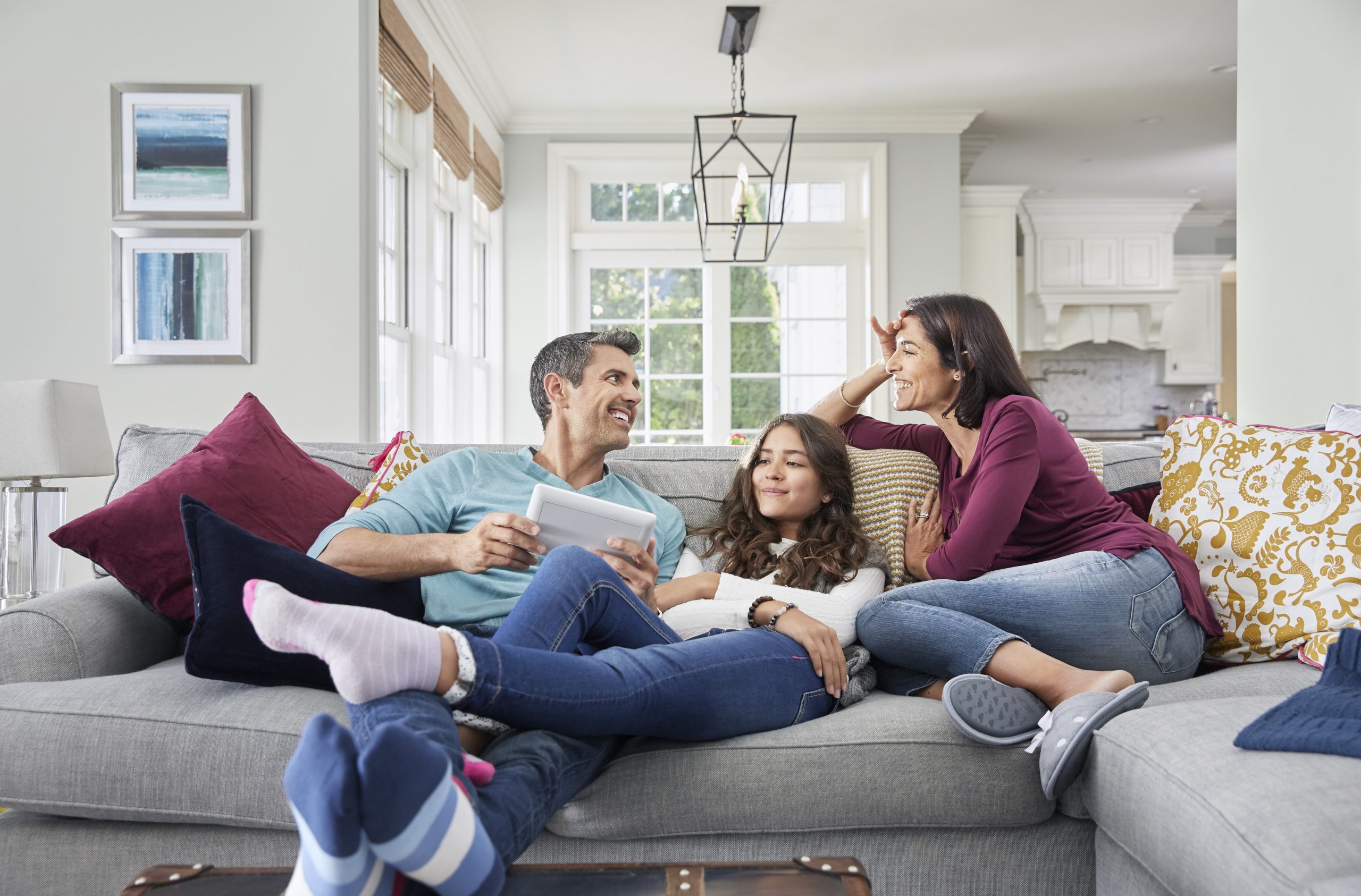 A happy family sits on their living room couch enjoying peace of mind with their security system and home automation