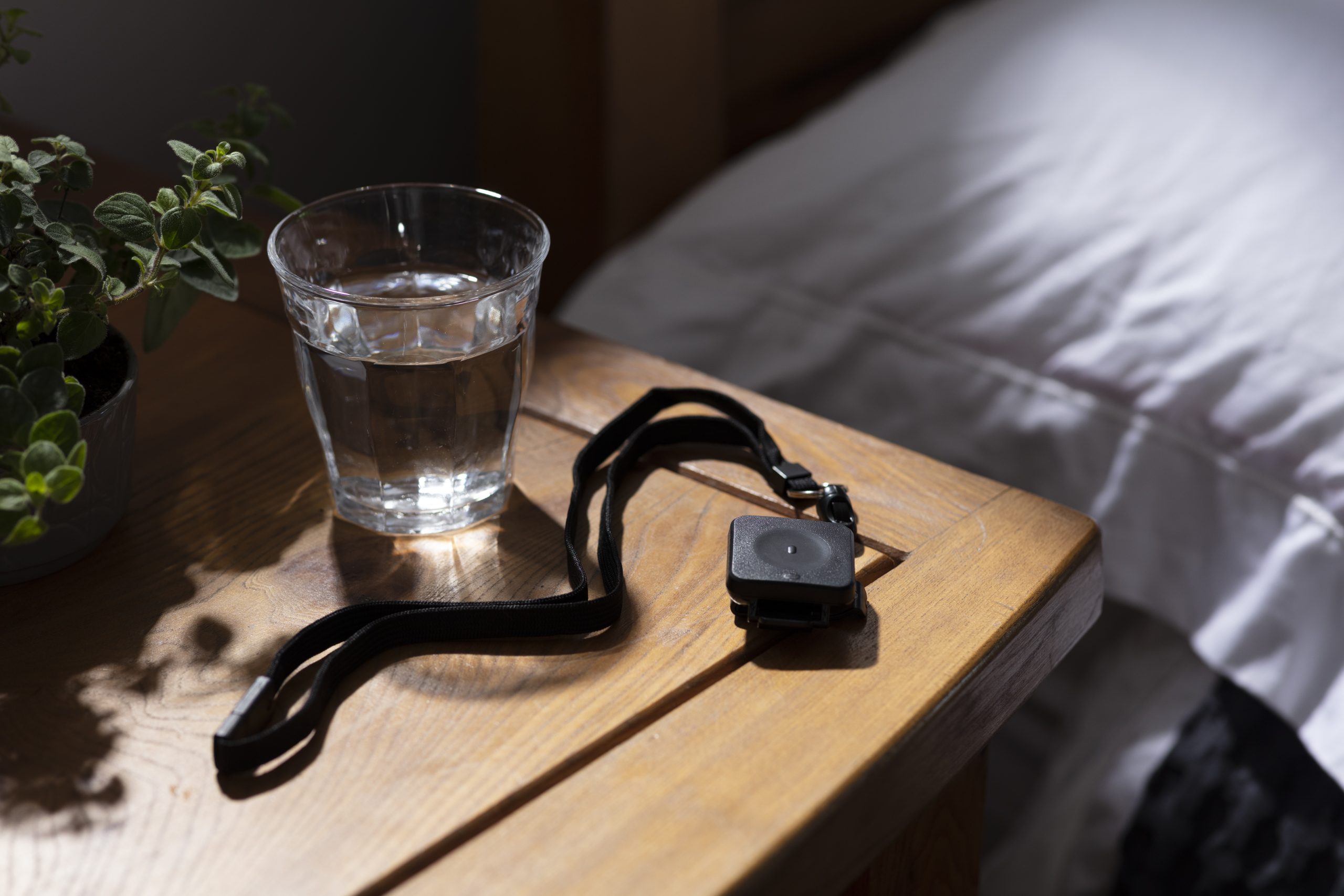A medical alert pendant on a nightstand next to a glass of water.