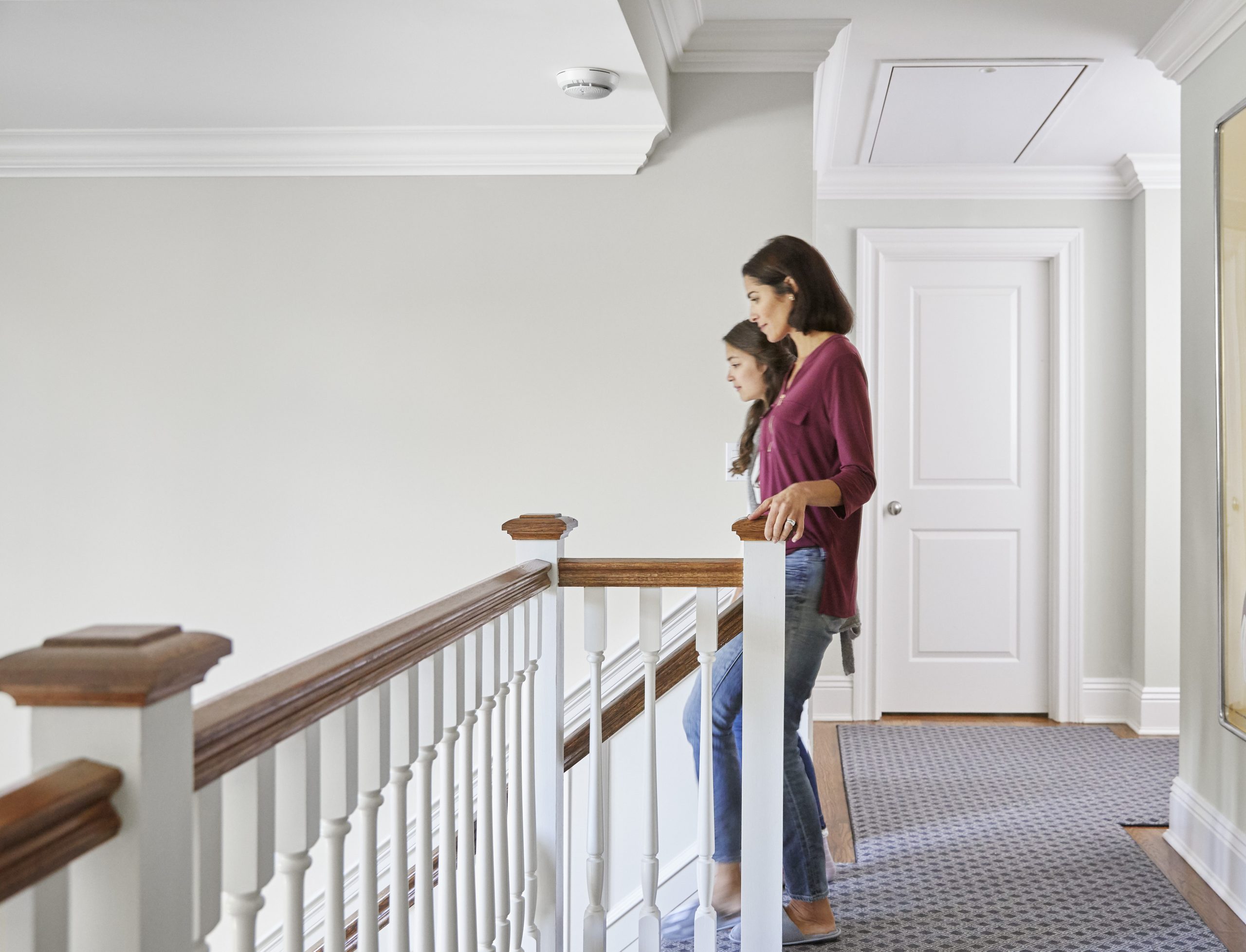 A woman and a girl walk down stairs with a carbon monoxide detector above them