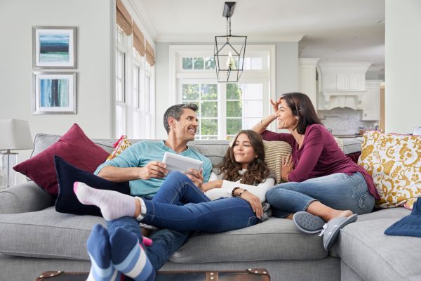 A family peacefully enjoys time together in their living room while observing the keypad of their home security system