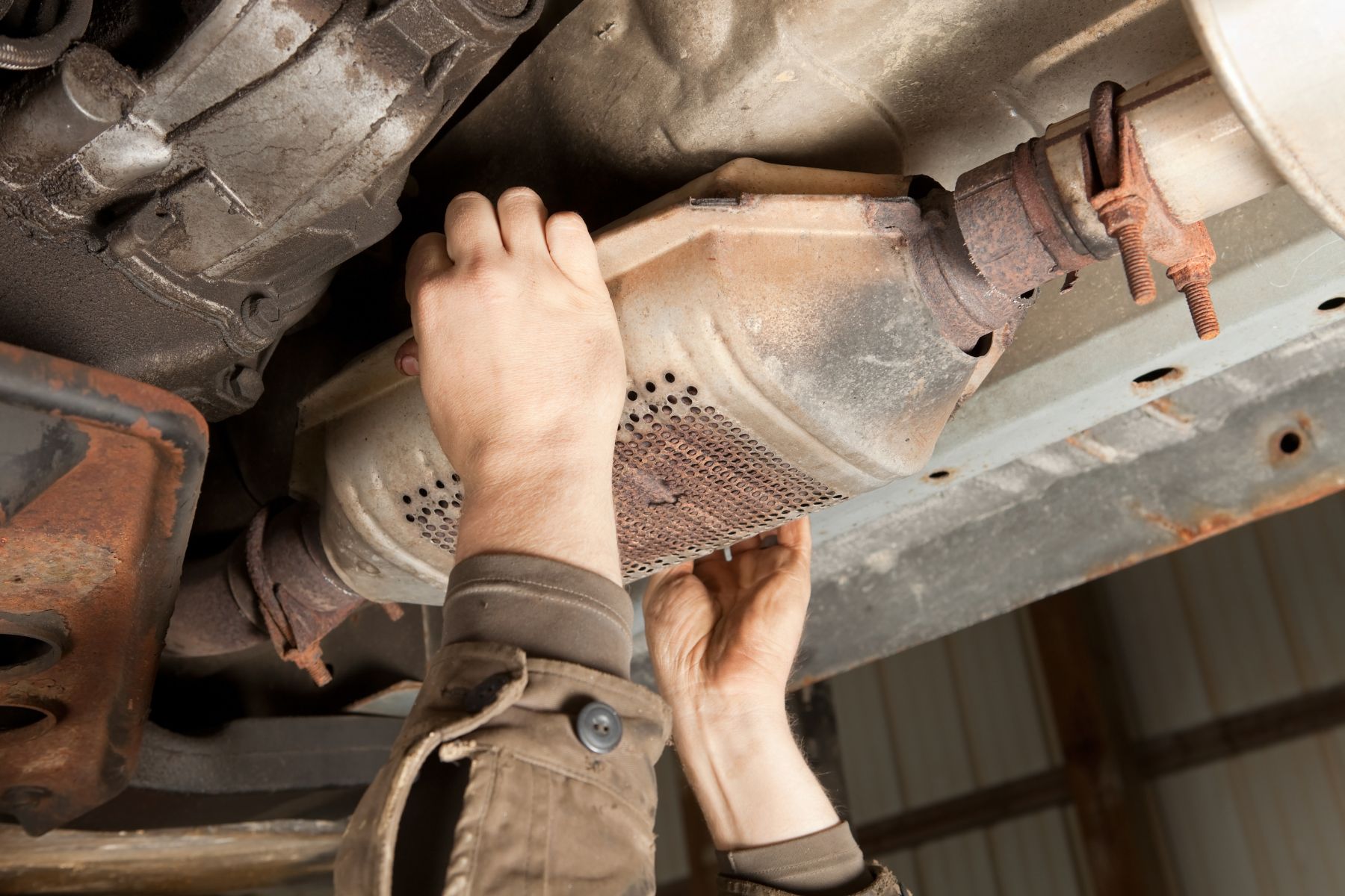 a persons hands on a cars muffler to get the catalytic converter. catalytic converter theft